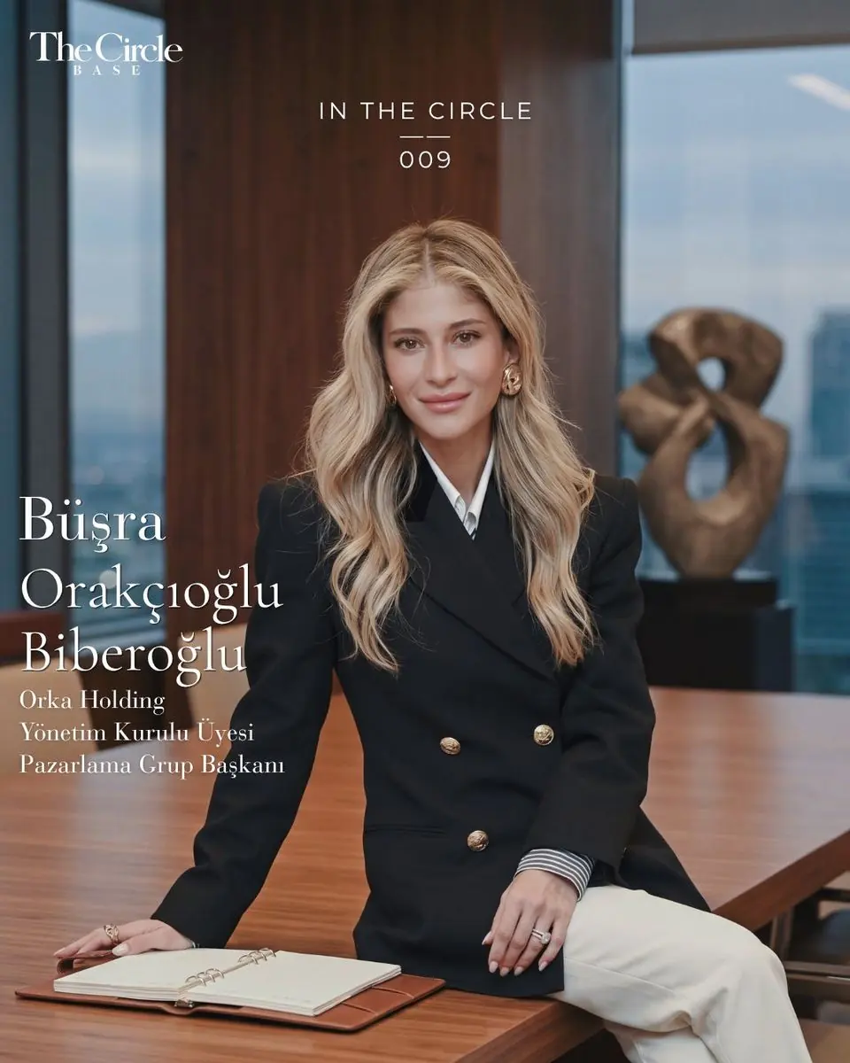 Büşra Orakçıoğlu Biberoğlu seated on a boardroom table in a black double-breasted blazer