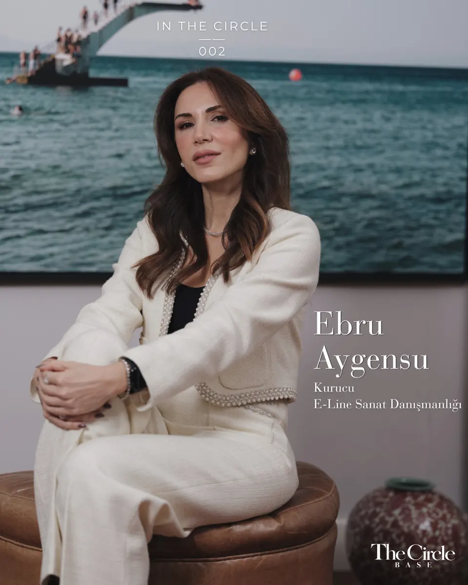 Ebru Aygensu in a cream tweed suit seated in front of a large sea photograph