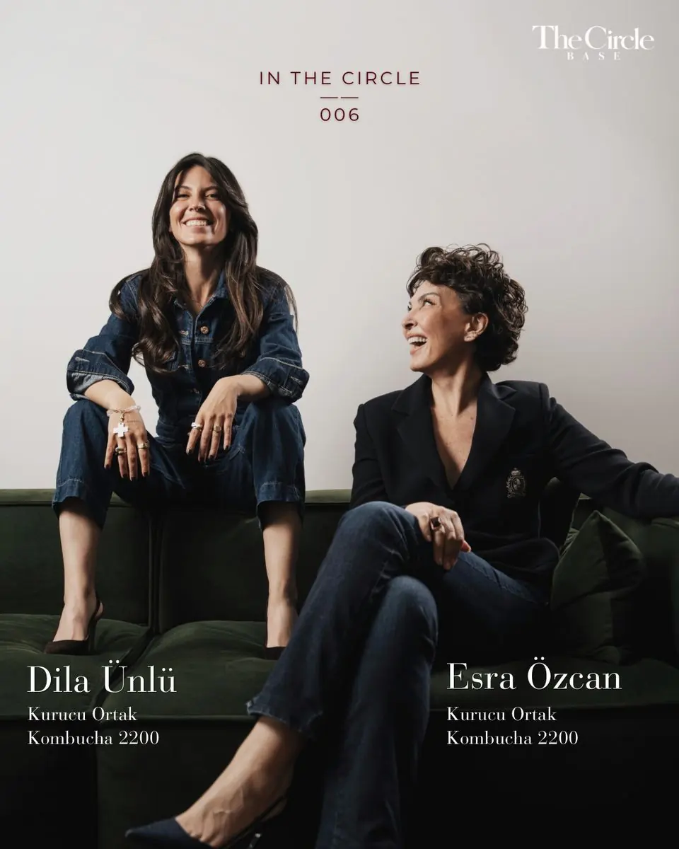 Dila Ünlü and Esra Özcan laughing together on a dark green sofa