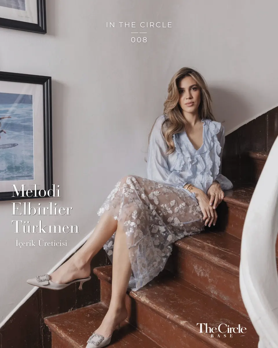 Melodi Elbirlier Türkmen seated on a wooden staircase in a pale blue ruffled blouse