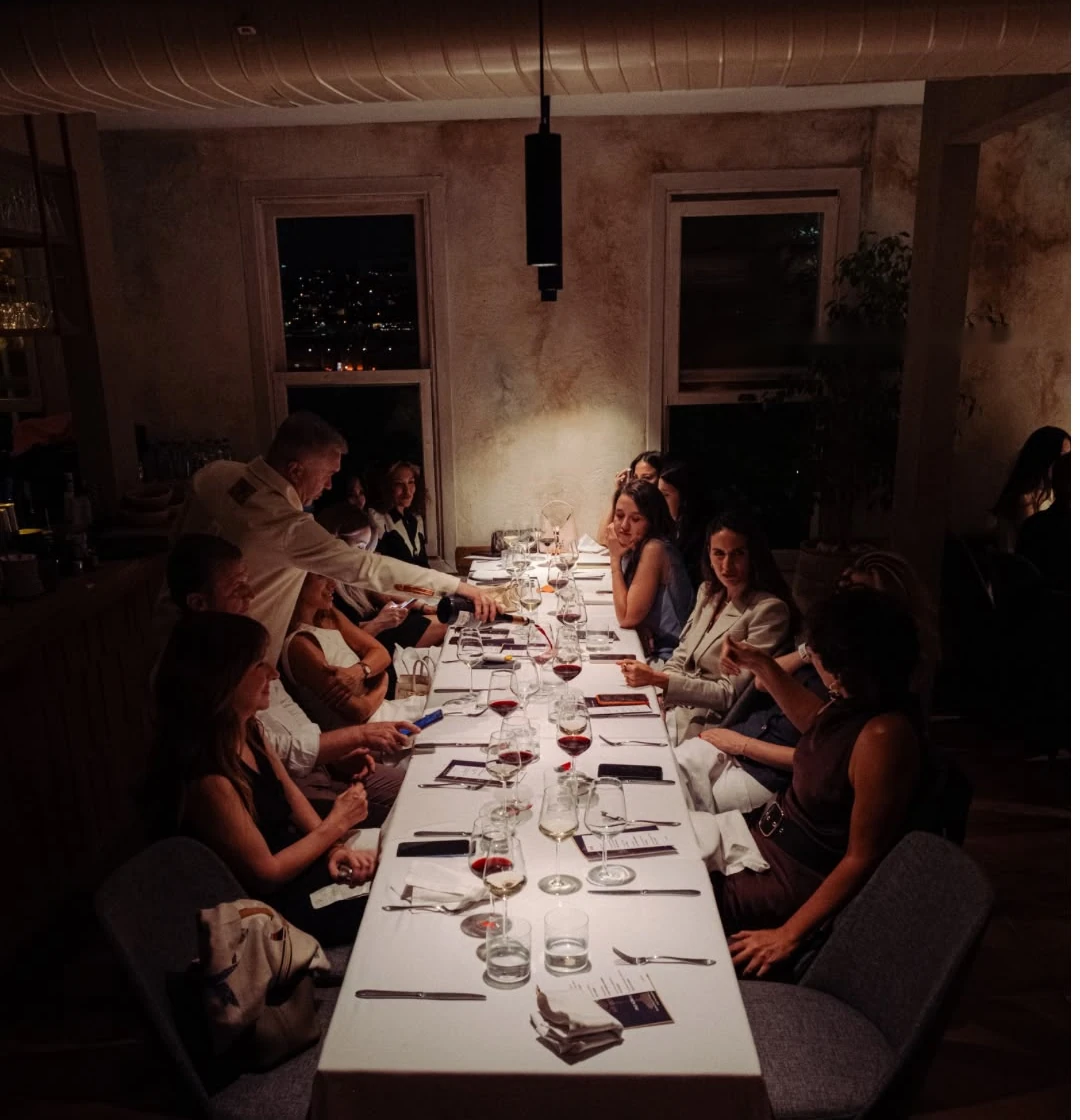 Guests along a long candlelit table, a host serving at the far end