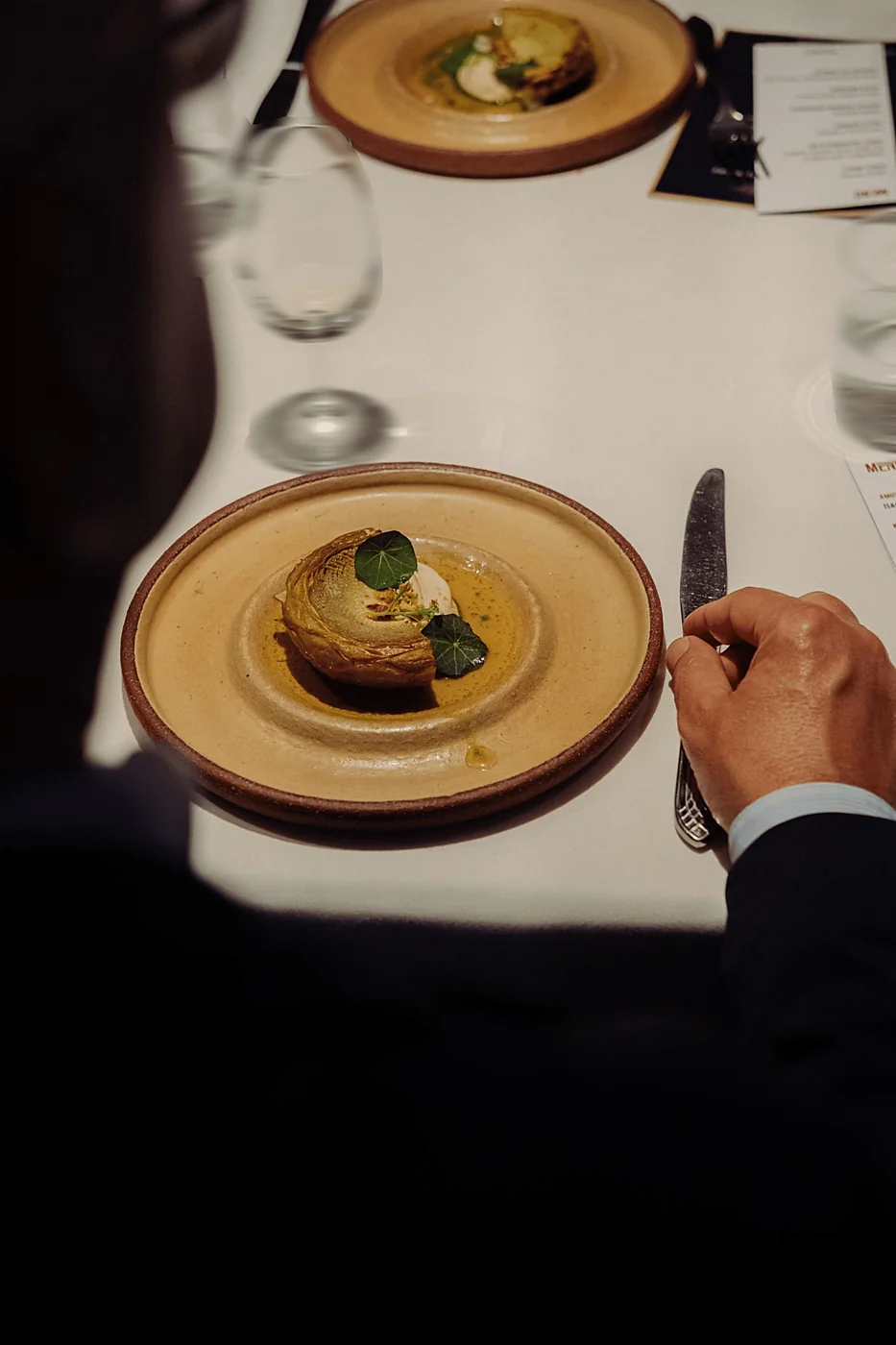 An overhead view of a plated course, a guest's hand resting by the knife