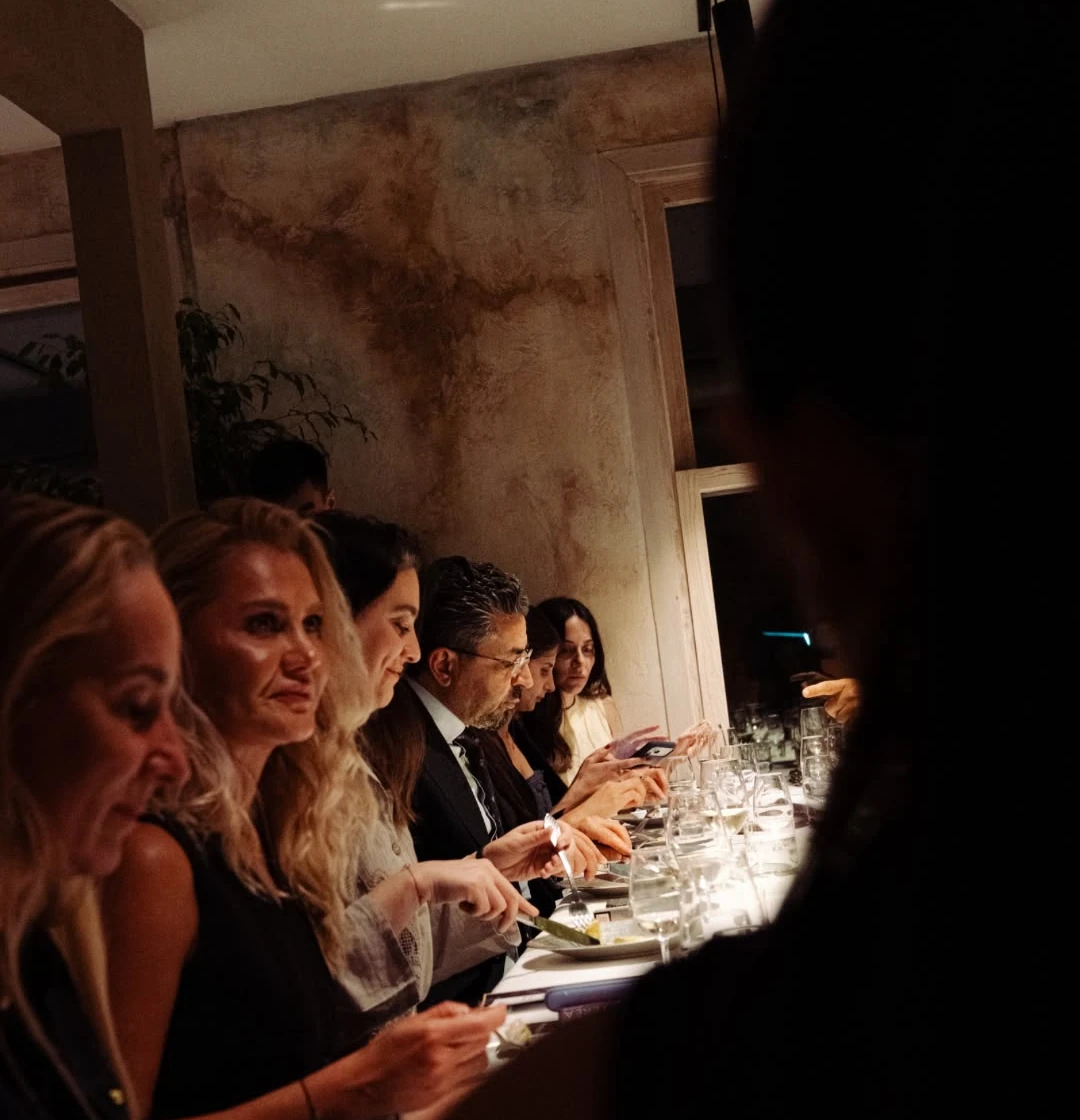 Guests dining along a candlelit table, faces lit by a single lamp