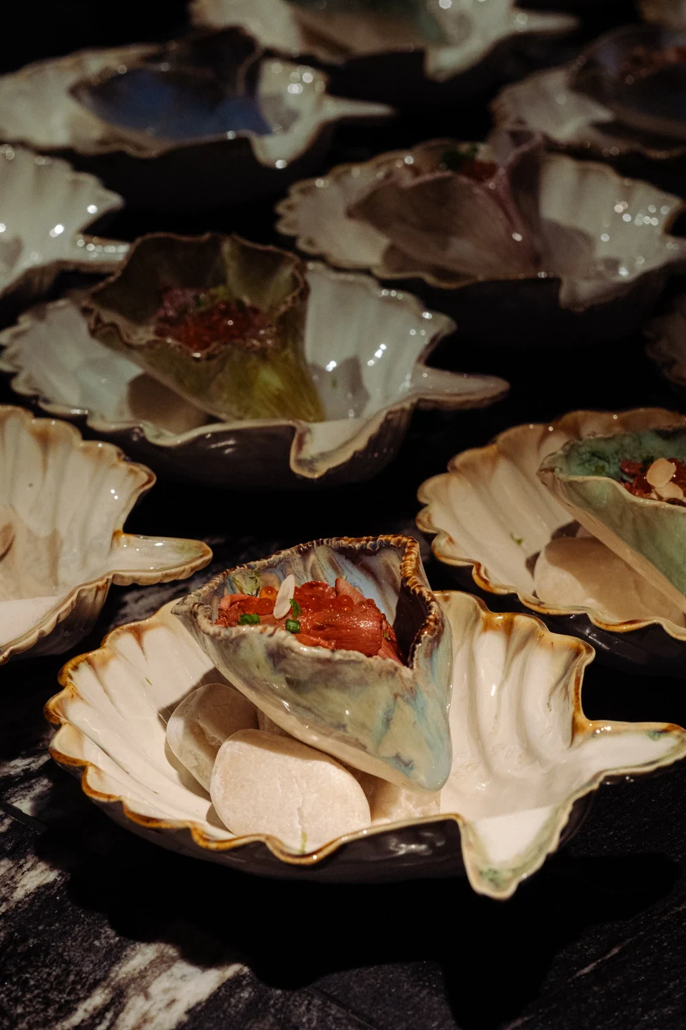 Shell-shaped dishes of small bites laid out on dark stone